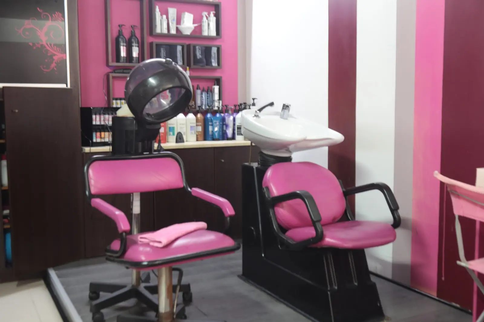 Interior do salão com cadeiras cor-de-rosa, secador de capacete e lavatório